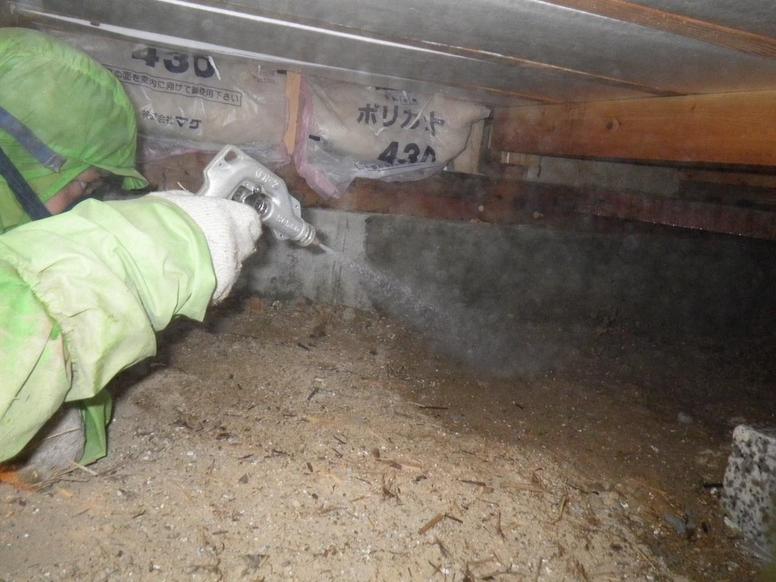 建物の床下の土壌に専門業者がシロアリ駆除の薬剤を散布する様子